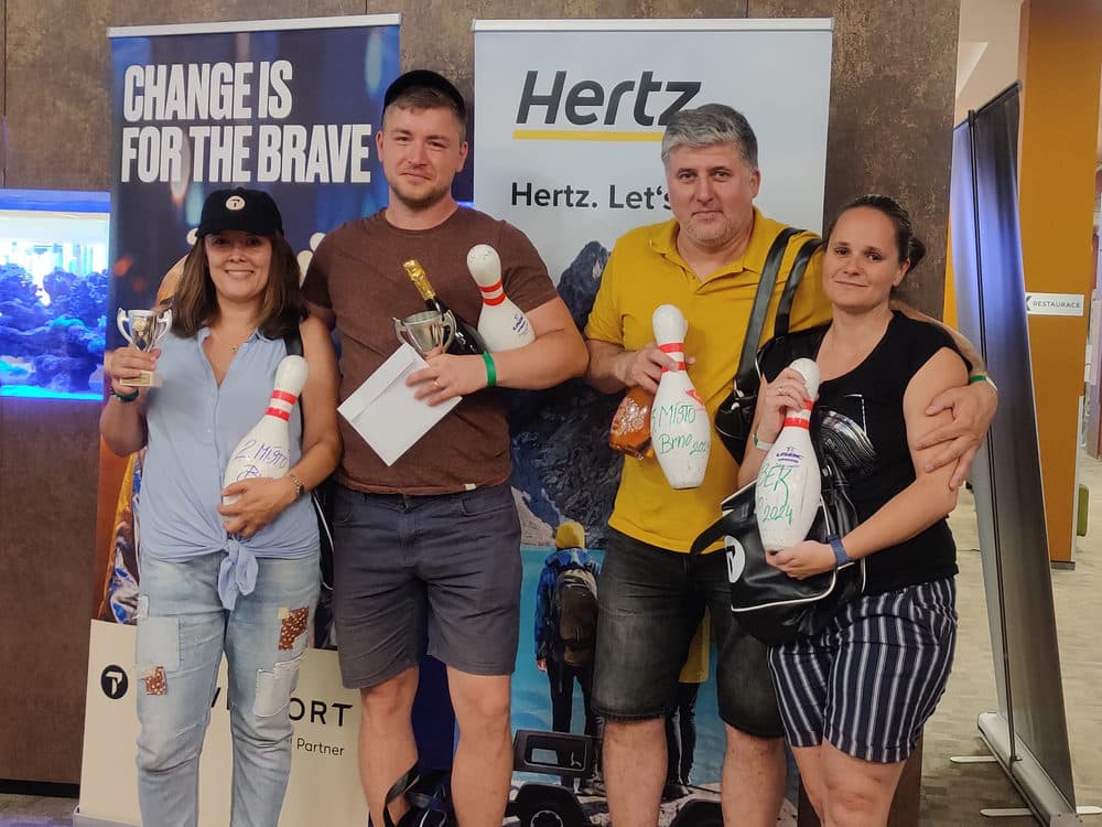 Víťazi brnianskeho bowlingu 2024 s pohármi a kolkami pred bannermi Hertz a Travelport
