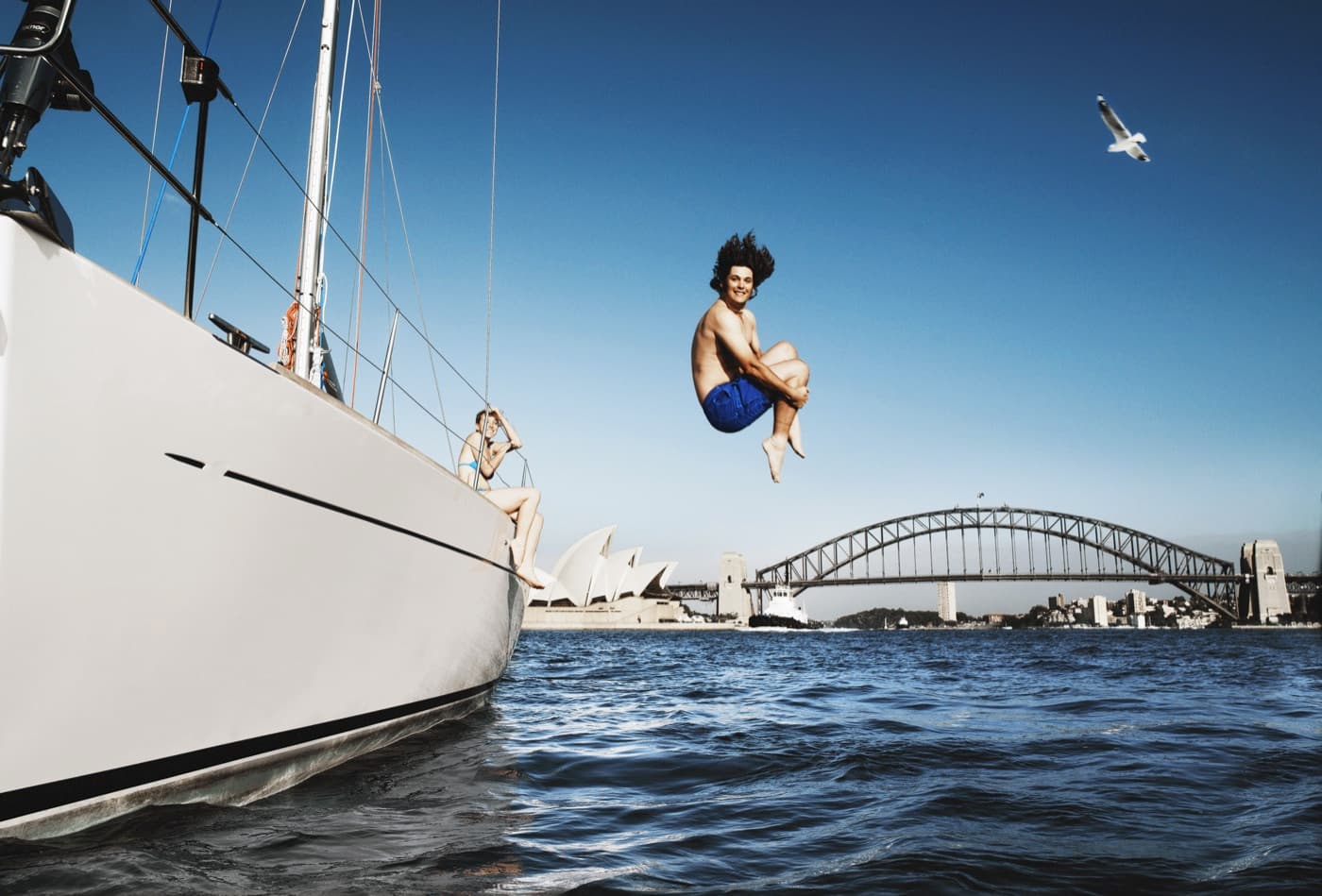 Mladý muž skáče z plachetnice do mora pred panorámou Sydney