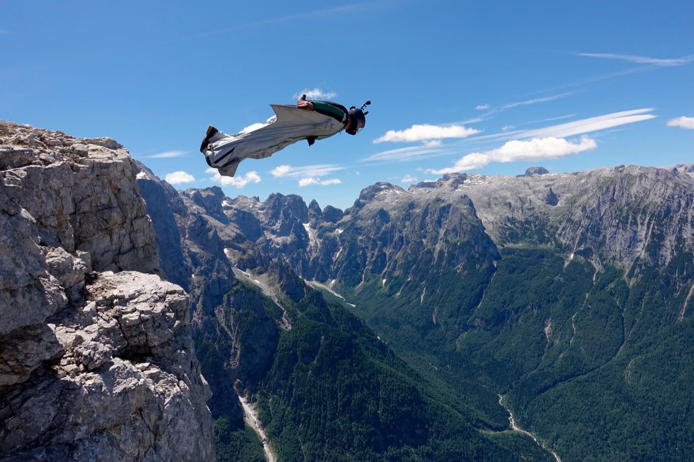 Wingsuitový letec skáče zo skalného útesu nad horským údolím