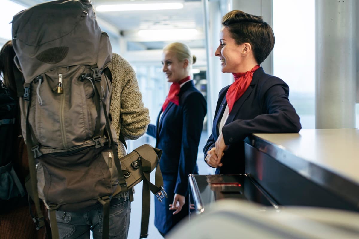 Usmiate letušky vítajú cestujúcich s batohmi pri odbavovacom pulte