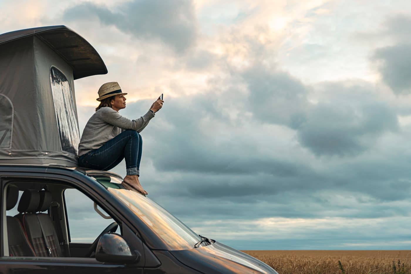 Žena fotografuje mobilom večernú krajinu zo strechy obytného vozidla