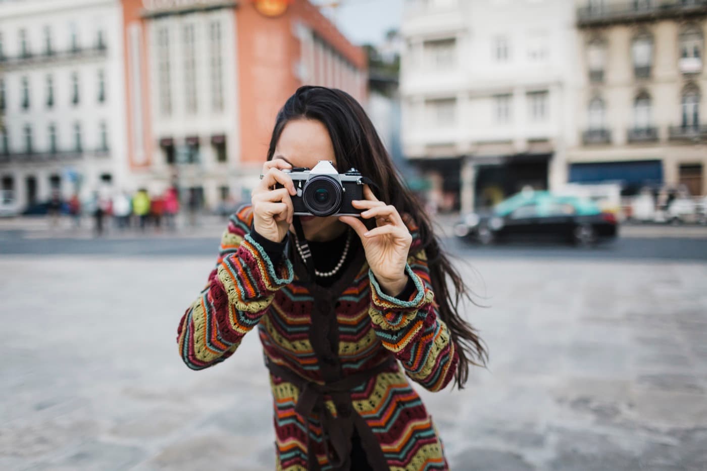 Fotografka v pestrom svetri mieri objektívom analógového fotoaparátu priamo na diváka